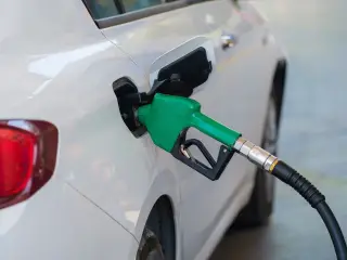 Ilustrasi: Nozel pompa bensin hijau sedang mengisi bahan bakar ke tangki mobil putih.