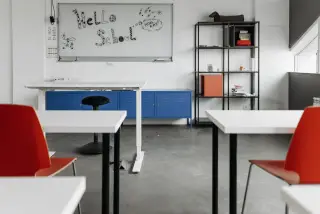 Ilustrasi: Ruang kelas kosong dengan deretan meja, kursi, dan papan tulis bertuliskan Hello School.