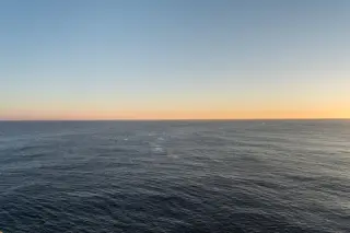 Ilustrasi: Pemandangan laut lepas dengan garis cakrawala di bawah langit senja yang bersih.