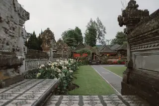 Ilustrasi: Kompleks pura Bali dengan taman berumput, tanaman bunga, dan dinding berukir.