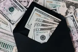 Ilustrasi: Uang kertas dolar Amerika Serikat di dalam amplop hitam di atas tumpukan lembaran uang kertas lainnya.