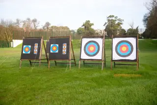 Ilustrasi: Empat papan target panahan berdiri di atas lapangan rumput terbuka.