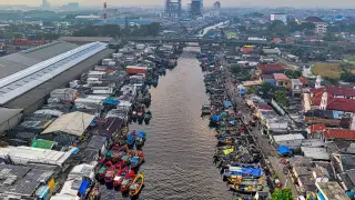 Ilustrasi: Pemandangan udara kanal permukiman padat dengan jajaran perahu nelayan yang bersandar.