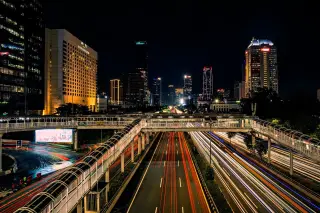 Ilustrasi: Pemandangan malam jalan raya perkotaan dengan jejak cahaya kendaraan dan gedung tinggi.