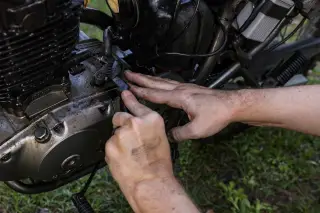 Ilustrasi: Sepasang tangan mekanik sedang membersihkan bagian mesin sepeda motor dengan sikat kecil.