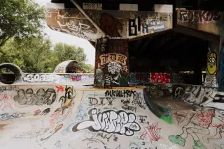Ilustrasi: Area skatepark beton di bawah jembatan yang dipenuhi berbagai coretan grafiti.