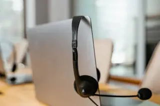 Ilustrasi: Headset hitam tergantung pada bagian belakang layar laptop di meja kantor.