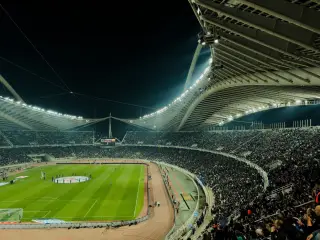 Ilustrasi: Pemandangan malam stadion sepak bola dan atletik yang dipadati penonton dengan lampu menyala terang.