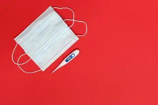 Ilustrasi: Masker medis dan termometer digital di atas latar belakang merah polos.