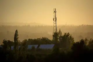 Ilustrasi: Menara telekomunikasi berdiri di antara pepohonan rimbun saat senja berkabut.
