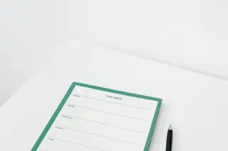 Ilustrasi: Buku agenda mingguan dan sebuah pena di atas meja putih.