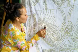 Ilustrasi: Seorang wanita sedang mencanting pola pada kain batik putih.