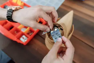 Ilustrasi: Tangan seseorang sedang merakit papan sirkuit elektronik mikro pada benda kayu.