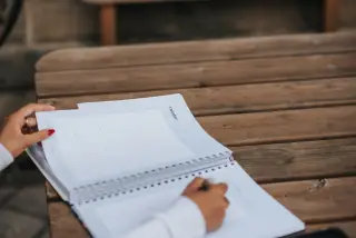Ilustrasi: Seseorang membuka buku agenda bertuliskan October di atas meja kayu.