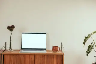 Ilustrasi: Sebuah laptop dengan layar menyala di atas meja kayu di samping cangkir dan tanaman hias.