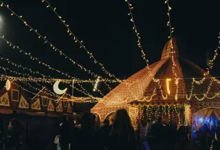 Ilustrasi: Tenda berhiaskan untaian lampu malam hari dengan siluet orang-orang yang melintas.