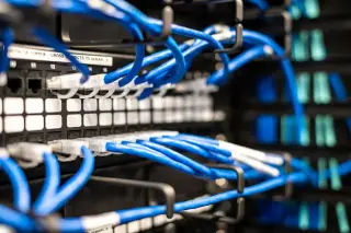 Ilustrasi: Deretan kabel jaringan biru yang terhubung ke panel server rak data.