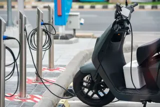 Ilustrasi: Sepeda motor listrik terparkir dan sedang diisi daya pada stasiun pengisian di tepi jalan.