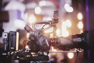 Ilustrasi: Kamera video profesional terpasang pada rig dengan latar belakang lampu bokeh.