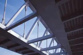 Ilustrasi: Struktur rangka baja modern dari bagian bawah jembatan dengan latar langit biru.