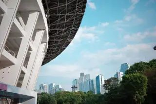 Ilustrasi: Struktur atap stadion modern dengan latar belakang gedung-gedung bertingkat dan pepohonan di Jakarta.