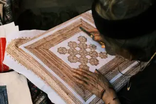 Ilustrasi: Seorang perajin sedang menggambar pola tradisional pada kain putih dengan alat khusus.