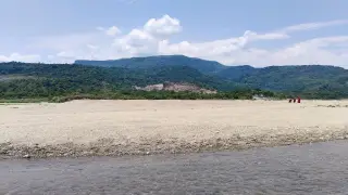 Ilustrasi: Sungai berpasir dangkal dengan latar belakang perbukitan hijau dan langit berawan.
