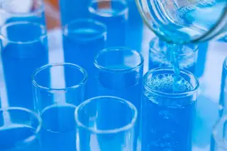 Ilustrasi: Cairan biru dituangkan ke dalam deretan tabung reaksi kaca di laboratorium.