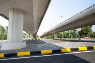 Ilustrasi: Jalan aspal mulus dan jalur layang beton yang ditopang tiang-tiang besar di area berpohon.