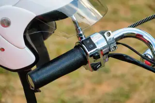Ilustrasi: Setang sepeda motor berbalut kulit hitam dan helm putih dengan kaca pelindung.