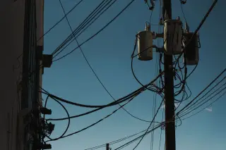 Ilustrasi: Tiang listrik dengan transformator dan kabel berseliweran berlatar langit biru.