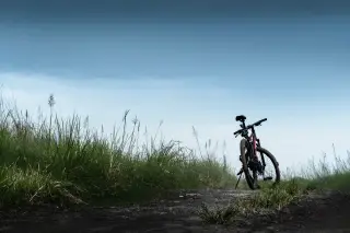 Ilustrasi: Sebuah sepeda gunung terparkir di jalur tanah berumput di bawah langit cerah.
