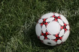 Ilustrasi: Sebuah bola sepak bermotif merah dan hitam tergeletak di atas rumput hijau.