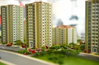 Ilustrasi: Maket miniatur gedung apartemen dan kawasan perumahan bertingkat dengan pepohonan kecil.
