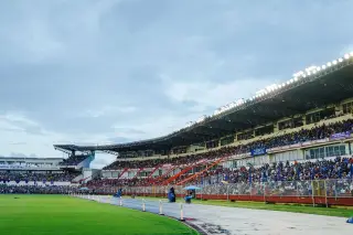 Ilustrasi: Tribun stadion olahraga yang dipadati penonton di bawah langit berawan.