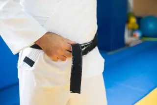 Ilustrasi: Seseorang mengenakan seragam judo putih sedang mengikat sabuk hitam di dalam ruangan.