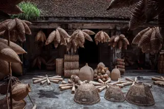 Ilustrasi: Berbagai kerajinan anyaman bambu tertata rapi di halaman depan sebuah bangunan tradisional beratap genteng.