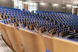 Ilustrasi: Deretan kursi biru kosong tersusun melingkar di dalam auditorium yang luas.