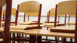 Ilustrasi: Deretan kursi dan meja kayu kosong di dalam ruang kelas.