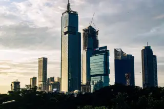 Ilustrasi: Deretan gedung pencakar langit dan proyek konstruksi dengan latar langit sore.
