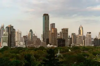 Ilustrasi: Pemandangan gedung pencakar langit kota modern di balik pepohonan taman kota.