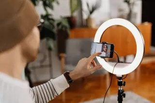 Ilustrasi: Seseorang sedang menyiapkan rekaman video dengan ponsel dan lampu cincin di dalam ruangan.