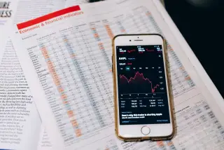Ilustrasi: Ponsel pintar menampilkan grafik pergerakan saham di atas lembaran data ekonomi.