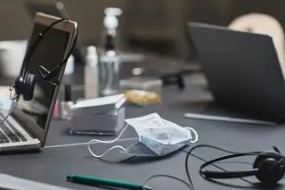 Ilustrasi: Masker medis, laptop, dan headset tergeletak di atas meja kerja.