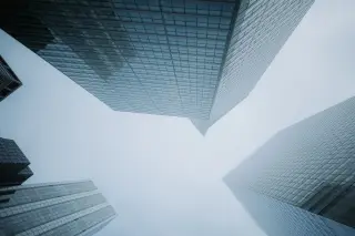 Ilustrasi: Sudut pandang rendah gedung pencakar langit berkaca dengan latar langit berkabut.