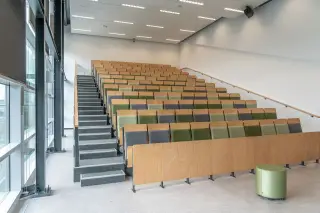 Ilustrasi: Deretan kursi kayu bertingkat di dalam ruang auditorium atau ruang kuliah yang kosong dan modern.