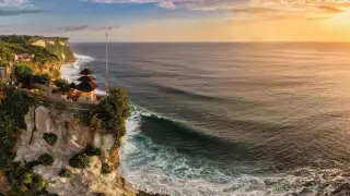 Ilustrasi: Pemandangan tebing dan pura di tepi laut Uluwatu saat senja.