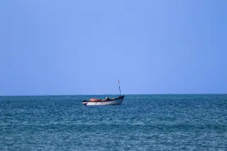 Ilustrasi: Sebuah perahu kecil terapung di tengah laut yang tenang di bawah langit biru cerah.