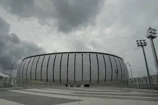 Ilustrasi: Stadion megah berfasad modern di bawah langit mendung berawan kelabu.