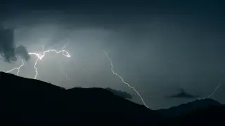 Ilustrasi: Kilatan petir menyambar di langit malam yang gelap di atas siluet perbukitan.